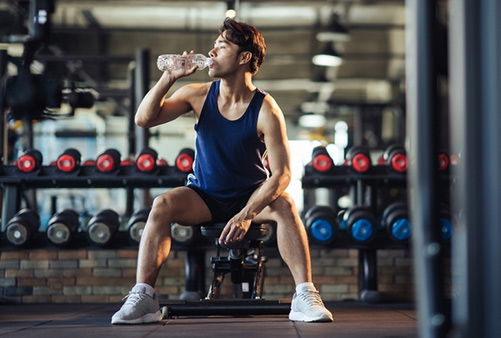 Man hydrating at gym, sitting on bench